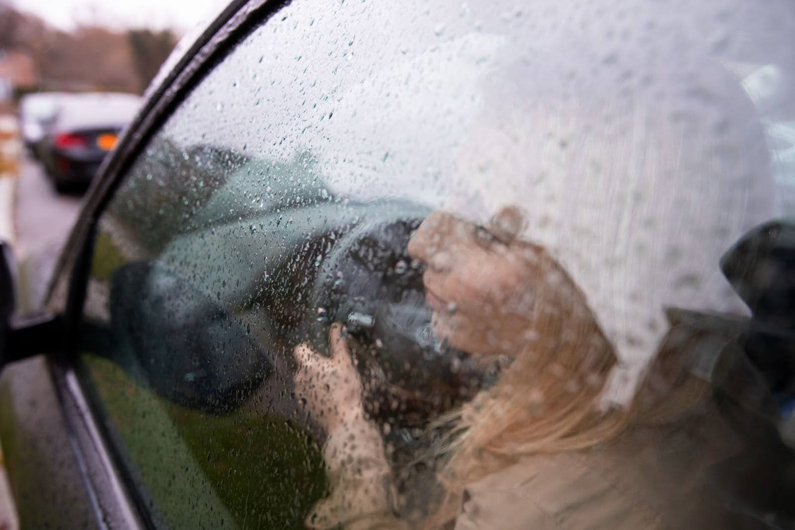 Visão de fora do carro, motorista loira olha para janela com o vidro embaçado fechado.