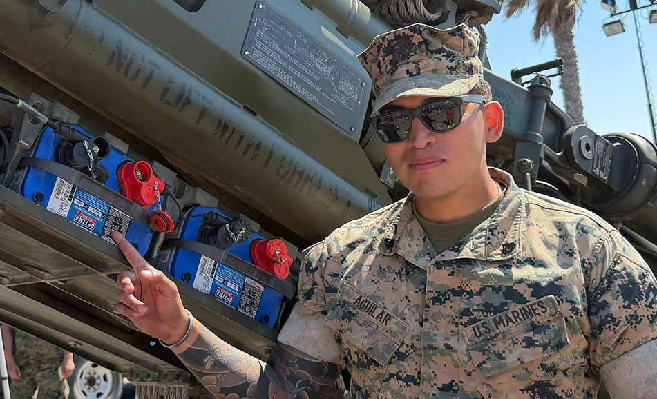 Soldier pointing at OPTIMA battery in military equipment.