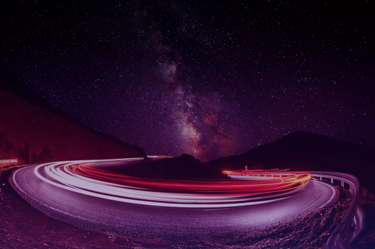 Distorted car lights around highway bend beneath starry night sky